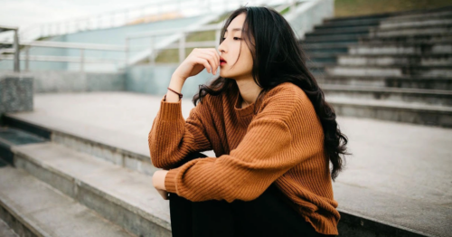 A teen in a brown sweater sits on bleachers