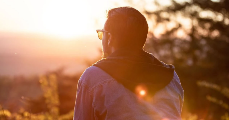 A man sits on a bench at sunset