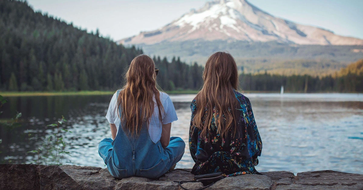 two women looking across a lake at a mountain talking about intergenerational trauma
