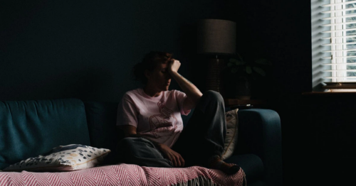 a teen dealing with depression sits on a couch in a dark room