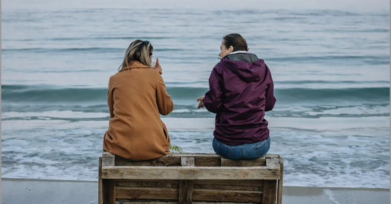 a couple sitting on a crate together looking out into the ocean