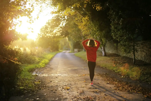 A female runner walks alone along a trail in the sun