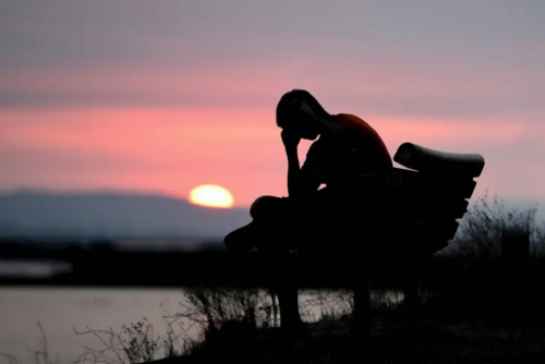 Teen depressed sitting on a bench alone at sunset