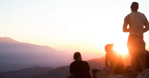 teens stand and talk together on a mountain at sunset