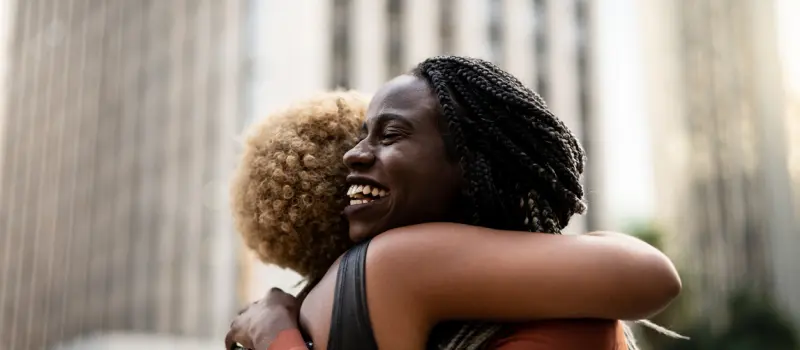 Two friends hugging and looking joyful.