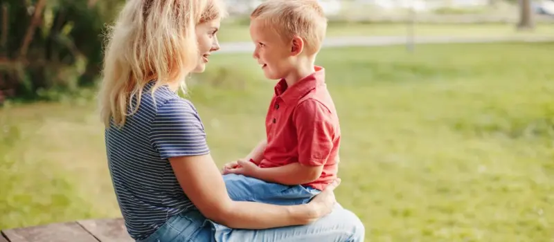 A little boy talking with his mom on her lap.