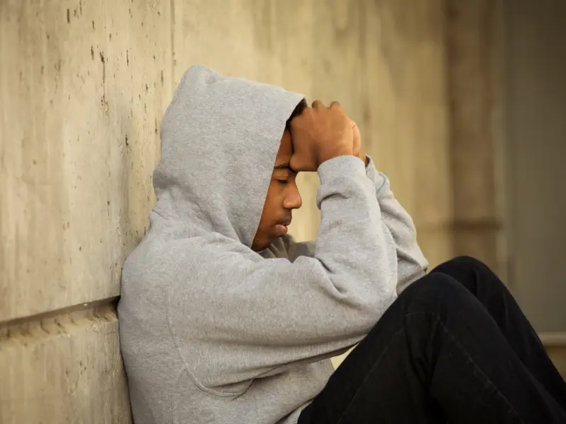 An individual wearing a grey hoodie is experiencing narcissistic abuse. He sits alone on the floor with his back to the wall