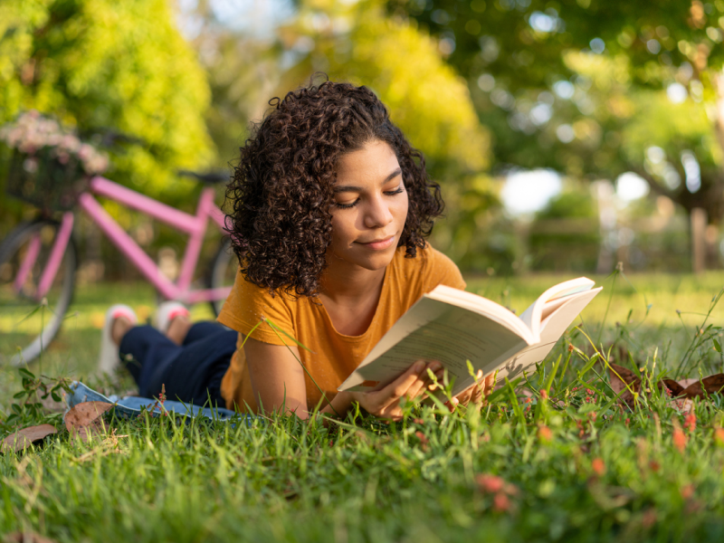 Teen reading outside during summer practicing self care