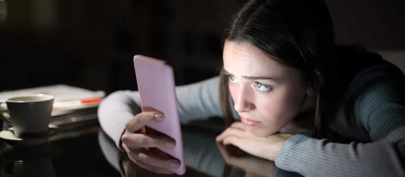 Teenage girl looking at her phone while dealing with depression. She could benefit from self-care.