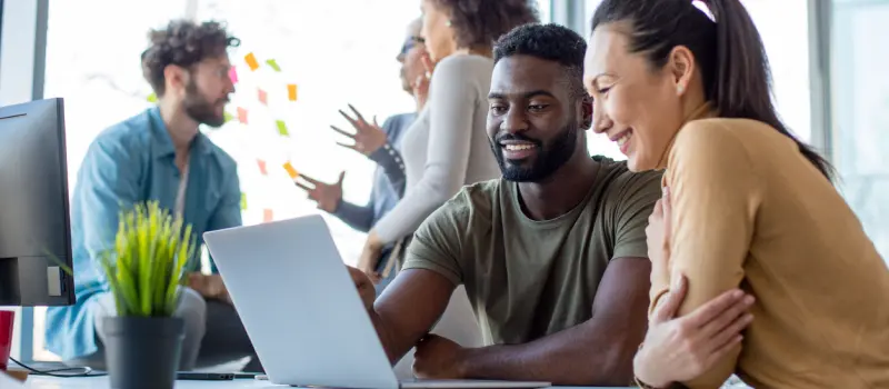 Male and female looking at a computer with other individuals behind them talking