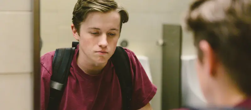 Male teen looking in the bathroom mirror at school