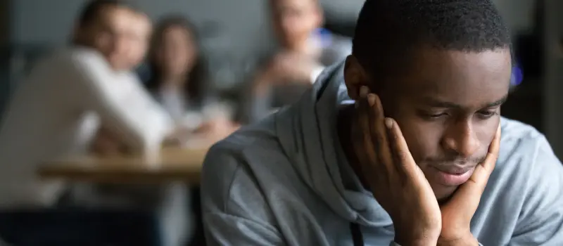 A young man with social anxiety sits isolated from his peers.