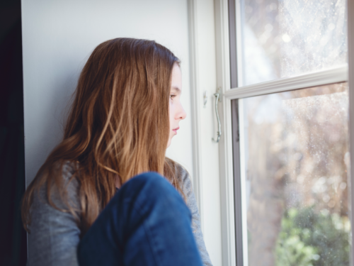 Teen girl looking out window dealing with depression