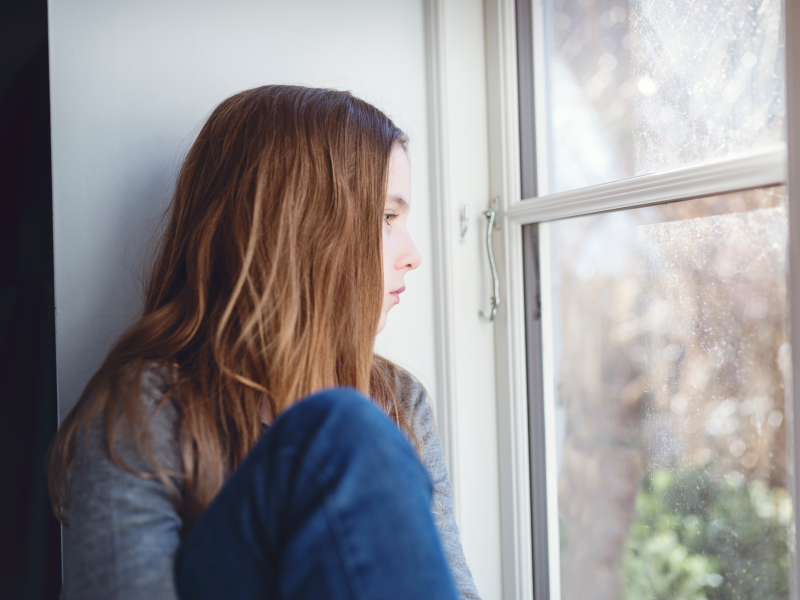 Teen girl looking out window dealing with depression