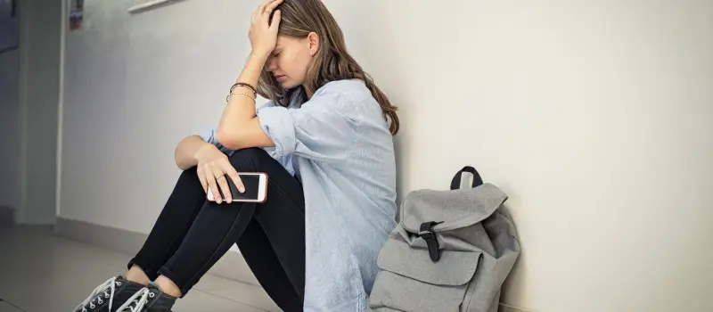 Teenage girl with depression up against a wall putting her hand on her head