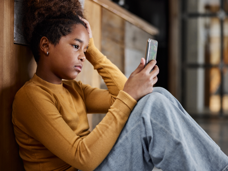 Young girl experiencing a depressive episode sitting down and looking at her phone