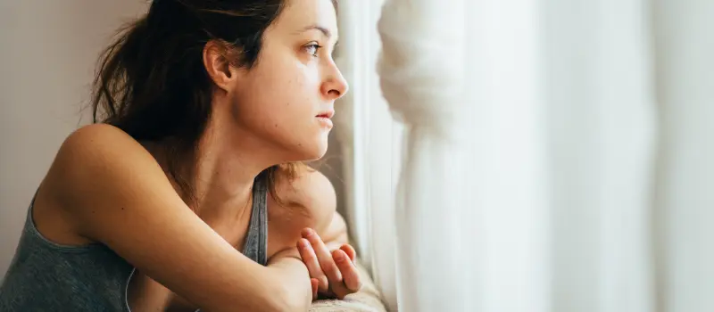 Woman on couch looking out a window dealing with bipolar disorder