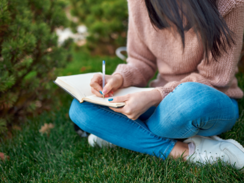 A teen girl struggling with depression and anxiety sits in the grass journaling about therapy