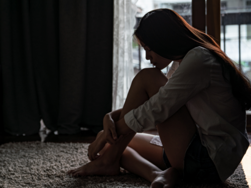Young person dealing with sexual assault sits in the dark alone