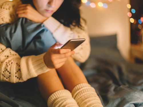 A teen girl sitting in her bedroom on her phone idealizes people on social media