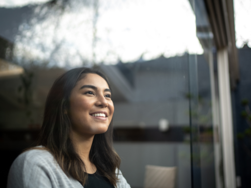 A young woman who has experienced trauma resilience smiles while looking out of a window