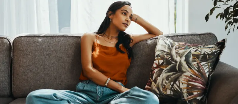 A young woman in an orange shirt sits on her couch after working through trauma resilience skills