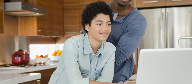 Teem and parent looking at a computer in the kitchen