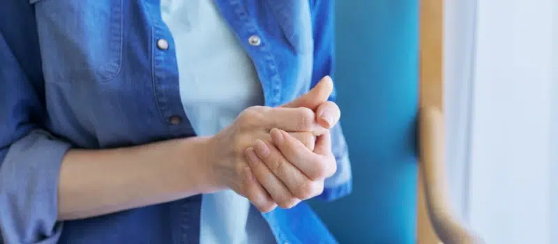 A person wearing a blue button up shirt tightly grips her hands as she deals with the symptoms of debilitating anxiety.