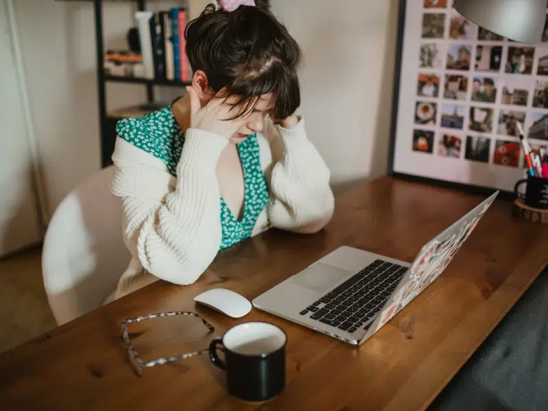 A person with debilitating anxiety sits at a desk holding her head as she struggles with symptoms.
