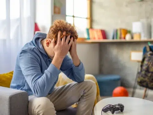 Young man with curly hair in a blue sweatshirt sits with his hands in his head dealing with hyper independence