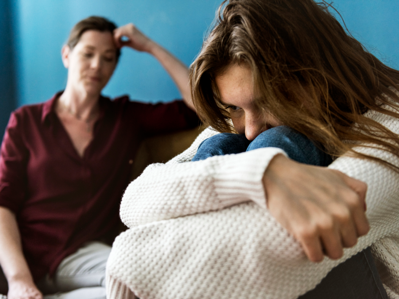 Teen dealing with severe anxiety in a fetal position while mom looks at her worried