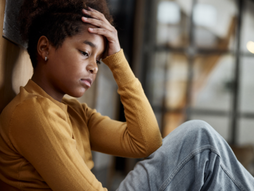 A teen girl in a yellow turtleneck sits alone struggling with serious mental health issues