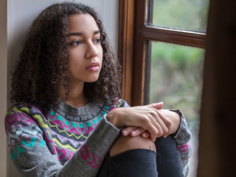 Teen with adhd sitting down looking out a window dealing with depression