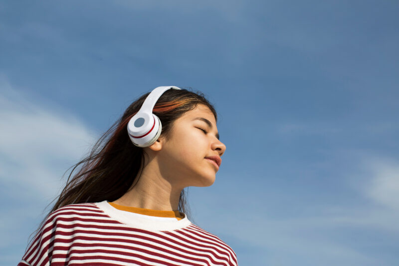 Beautiful girl with a headphones and colorful hair on a blue sky background