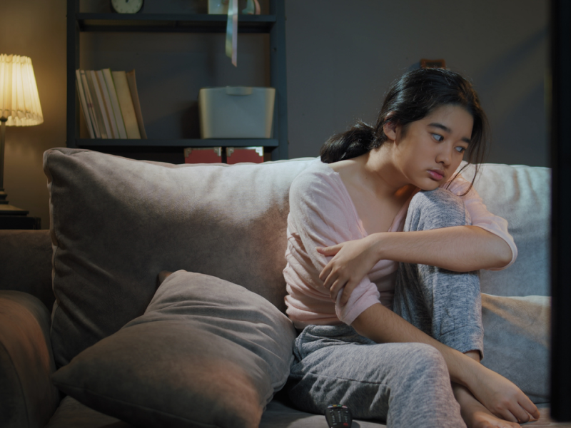 Teen girl sitting on a couch in a dark room having obsessive thoughts