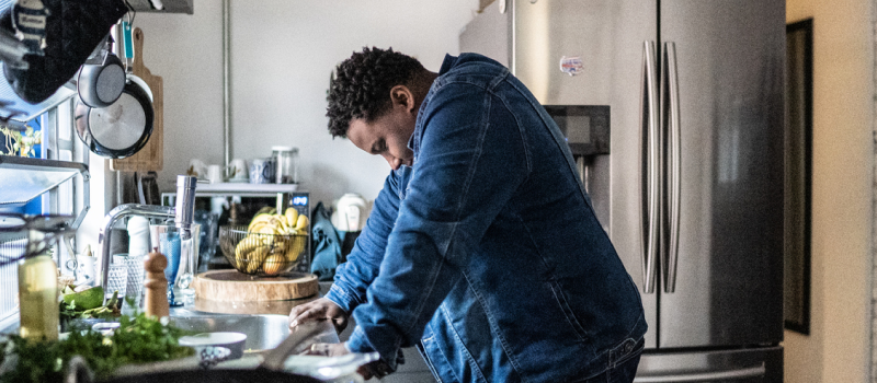 A person dealing with reactive abuse in his relationship stands over a sink thinking.