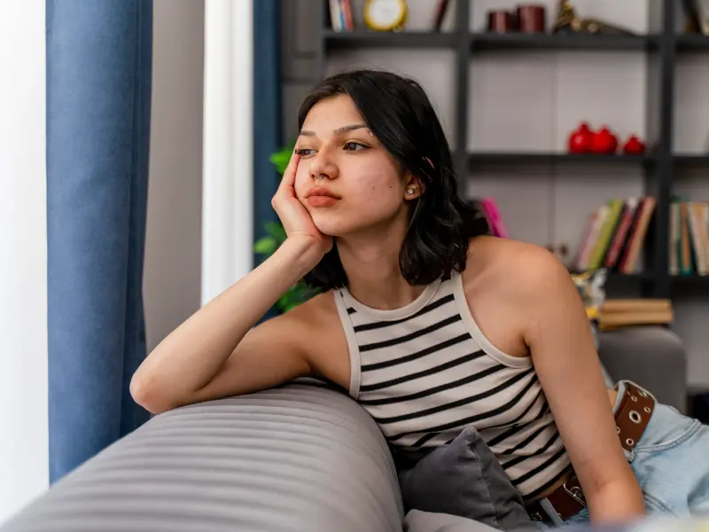 Young woman in striped tank top sitting on a couch struggling with mental health