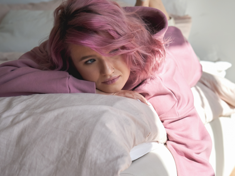 Young person with pink hair lays in bed dealing with a mood disorder