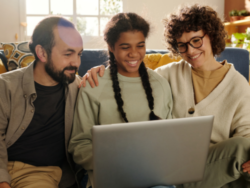 A young person participating in an intensive outpatient program sits in front of a computer with her smiling parents.