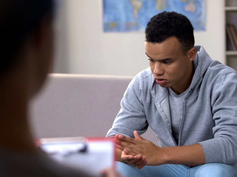 A person in a grey sweatshirt sits down during a therapy session. He is considering which form of therapy is best for him.