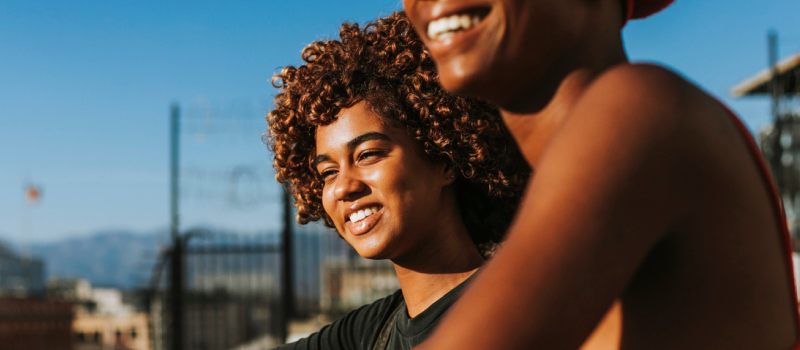 Two people stand smiling in front of a blue sky after using a guided meditation to help manage their PTSD symptoms.