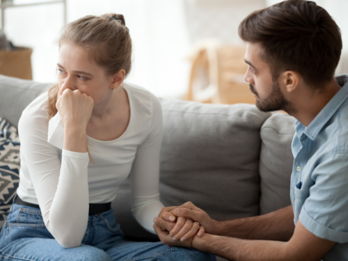 A woman in a white shirt cries while holding the hand of her partner with whom she is codependent.