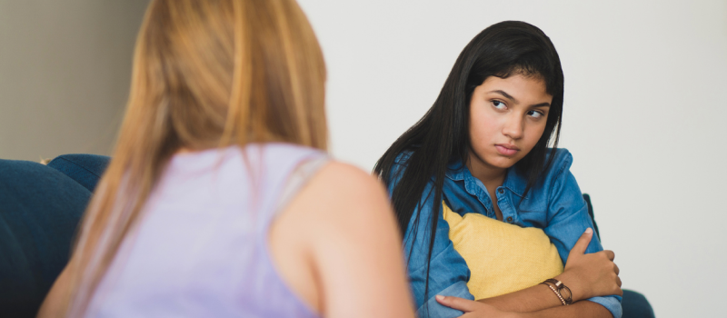 A young person in a blue shirt dealing with overstimulation holds a pillow to calm down during a therapy session.