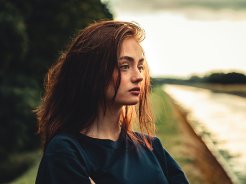 A young woman dealing with paranoid ideation as a result of paranoid personality disorder looks out into the distance with her arms crossed.