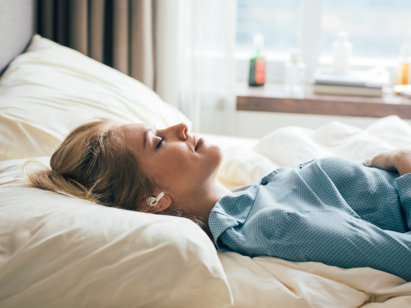 A person lies in bed in a blue shirt with a smile on her face as she calms her body and mind with a guided meditation for nighttime anxiety.