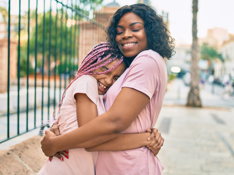 A parent and child wearing pink shirts embrace after a teen family therapy session that strengthened their relationship.
