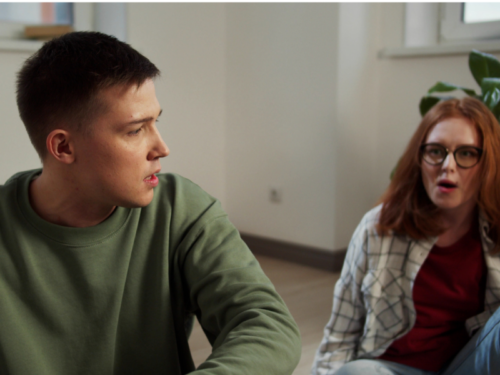 A man in a green long sleeve shirt who is dealing with complex PTSD in his relationship sits next to his partner who has red hair.
