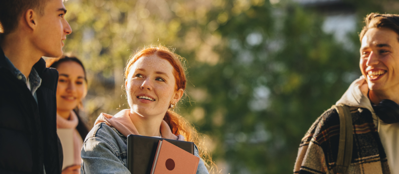 A group of people walk on a tree-lined street smiling. One with red hair carries books—she has struggled with anxiety and OCD in the past but is learning to cope with counterconditioning.