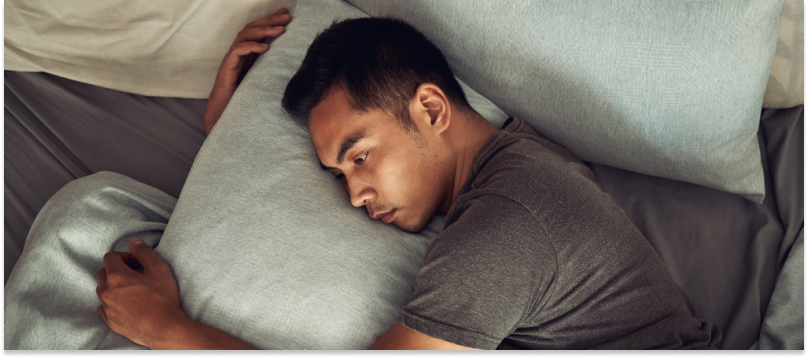 A young person lies in bed holding a pillow wondering to himself: "Why am I anxious at night?"