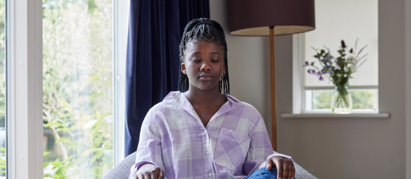 A person in a purple checkered shirt sits with her hands on her knees as she practices meditation to manage a panic attack.